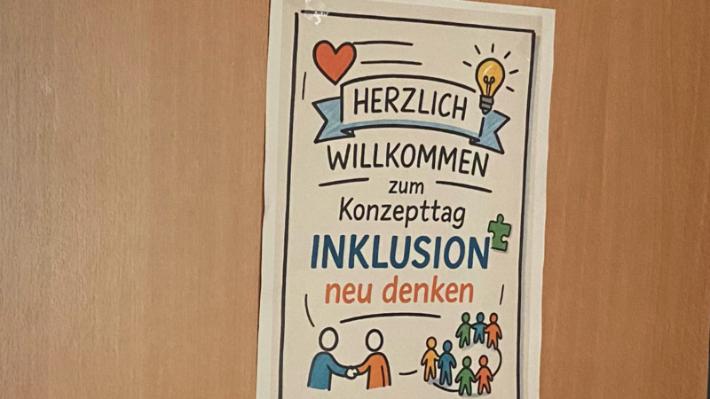 Auf dem Foto ist ein Plakat zu sehen, das an einer Tür oder Wand hängt. ?️ Was das Plakat sagt: Titel: HERZLICH WILLKOMMEN zum Konzepttag INKLUSION Untertitel: neu denken Bildelemente: Ein rotes Herz. Eine leuchtende Glühbirne (Symbol für eine neue Idee). Eine Sprechblase oder ein Banner mit der Aufschrift "HERZLICH WILLKOMMEN". Ein Puzzleteil (neben "INKLUSION"). Zwei Personen, die sich die Hand geben (symbolisiert Verbindung oder Zusammenarbeit). Eine Gruppe verschiedener, farbiger Strichmännchen (steht für Vielfalt und Gemeinschaft). Zusammenfassend: Es handelt sich um eine Einladung zu einem Konzepttag zum Thema Inklusion mit dem Motto, dieses Thema "neu zu denken". Sieht nach einem Tag voller Ideen aus – hoffentlich mit gutem Kaffee!